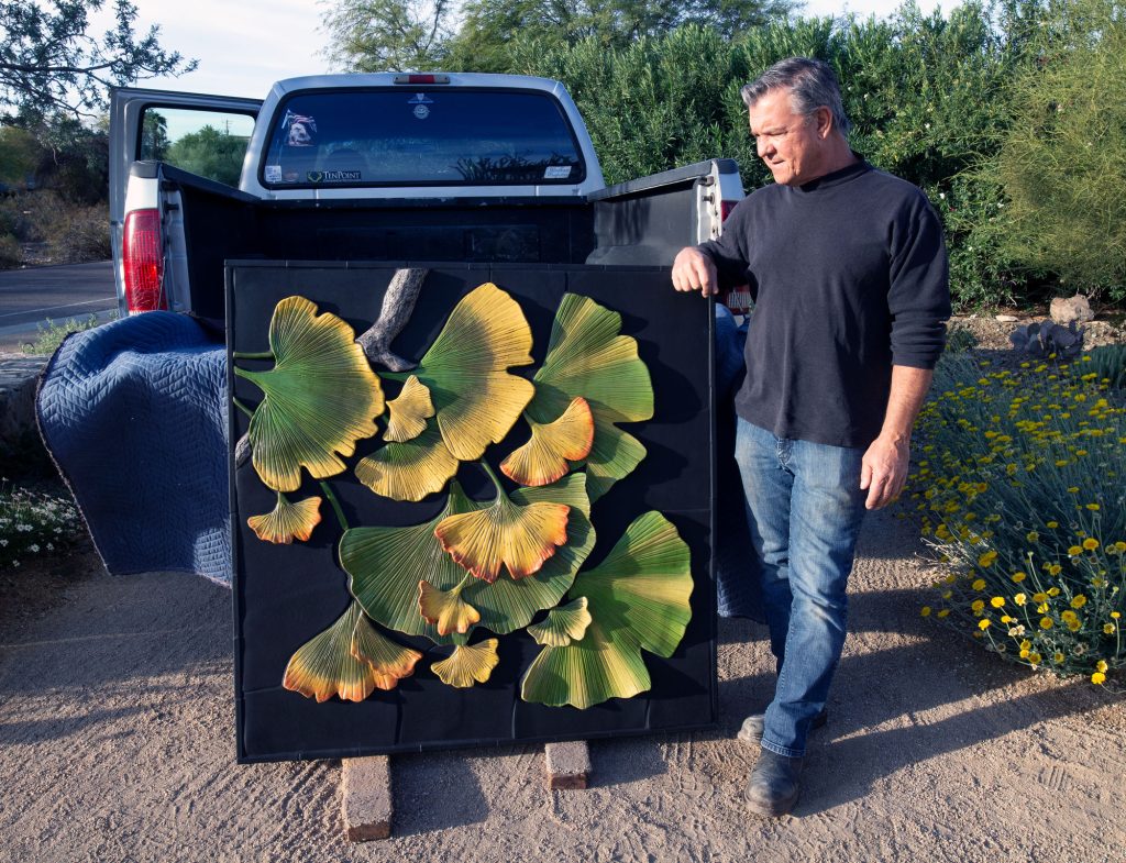 Man in jeans stands next to a ceramic wall art piece
