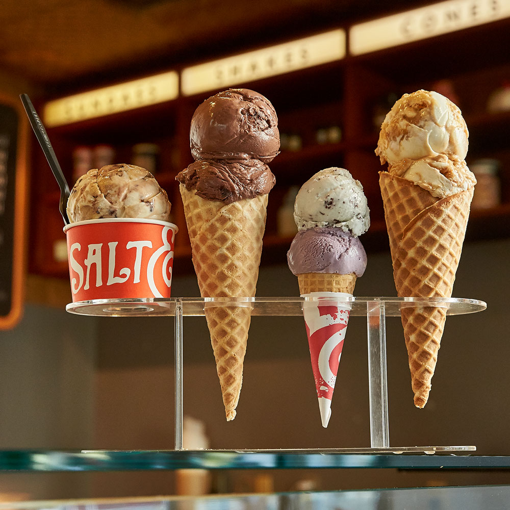 A cup of ice cream next to ice cream cones ini a stand