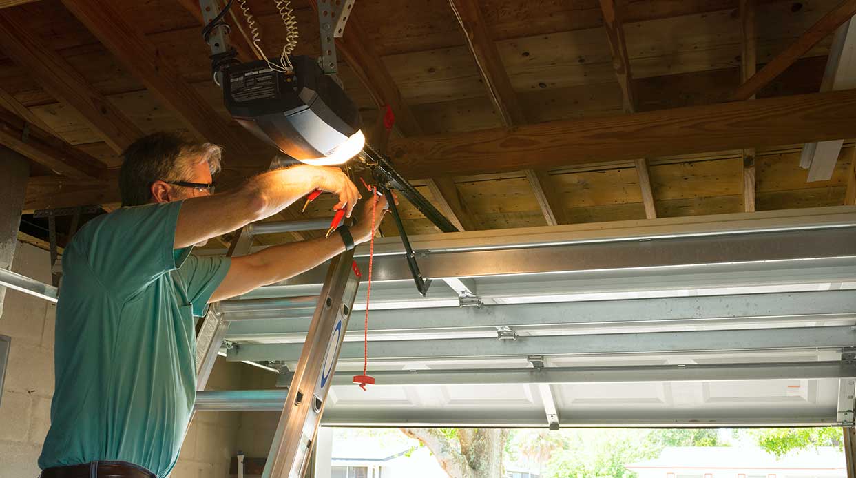 Professional automatic garage door opener repair service technician man working on a ladder at a home residential location making adjustments and fixing it while installing it.