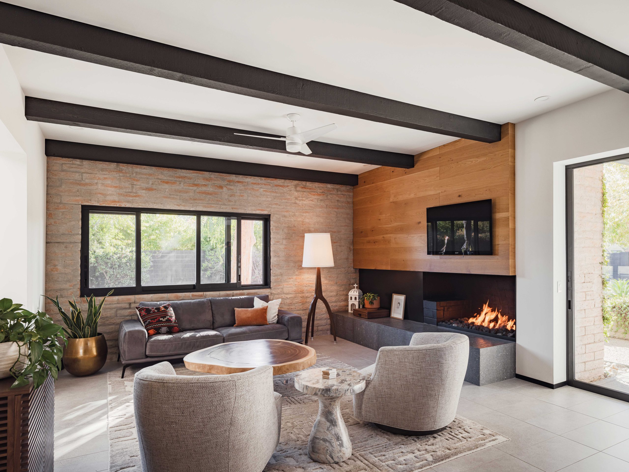 New cladding for the living room fireplace replaced the original heavy wood mantel. New black-framed windows and porcelain tile flooring update the space without diminishing the midcentury modern appeal.