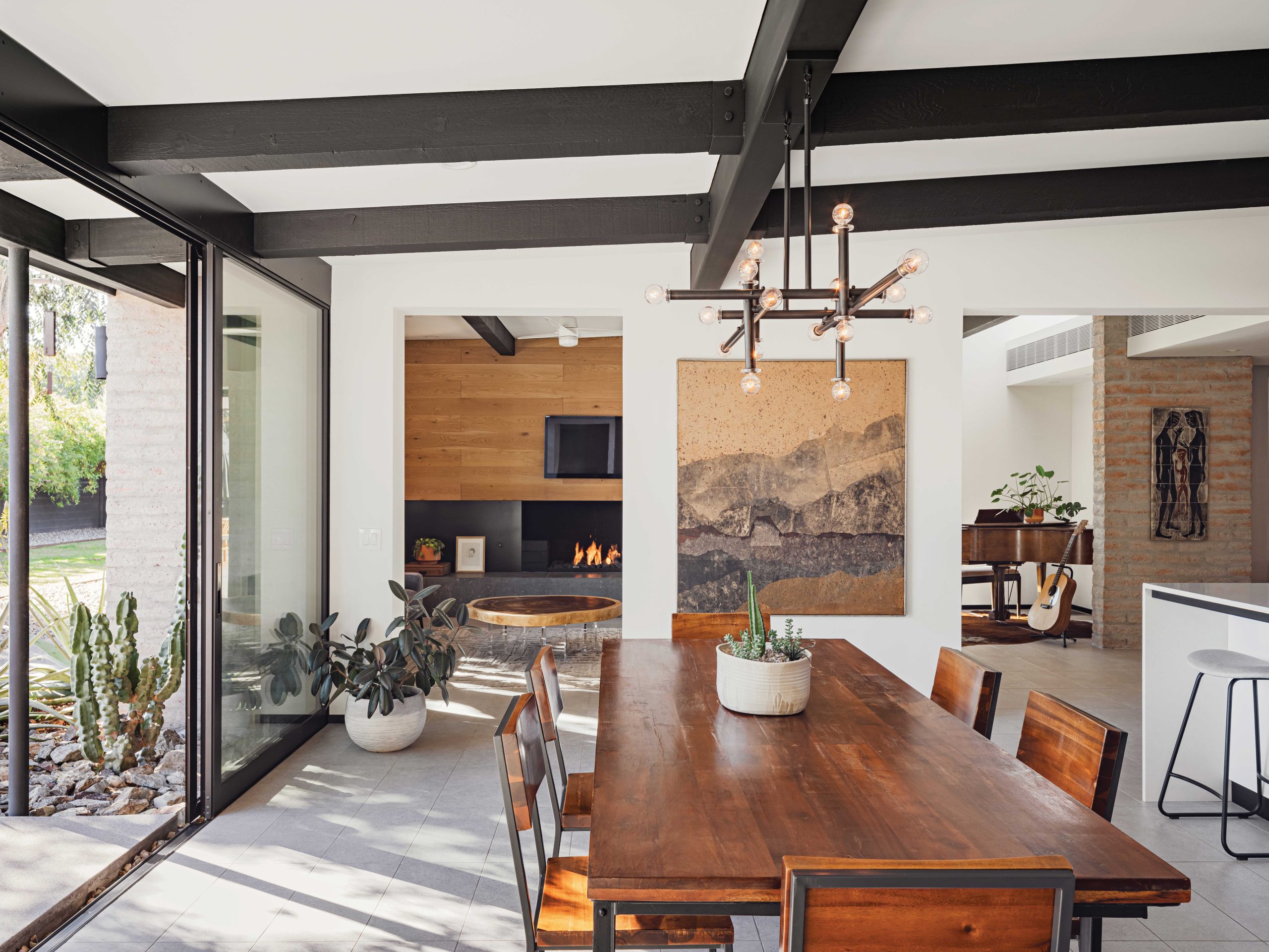 The architect and builder enclosed part of the back patio to create an expanded dining room that is still in scale with the home’s original dimensions. “Because we removed a load-bearing wall and added a glass wall to expand the dining room, we added a steel beam across the space for structural support,” explains Dan Noonan. “The original wood beams were white, but we painted them black to match the new steel beam.” At upper right, linear steel AC vents replaced the old standard single vents, reiterating the interior’s horizontal lines.