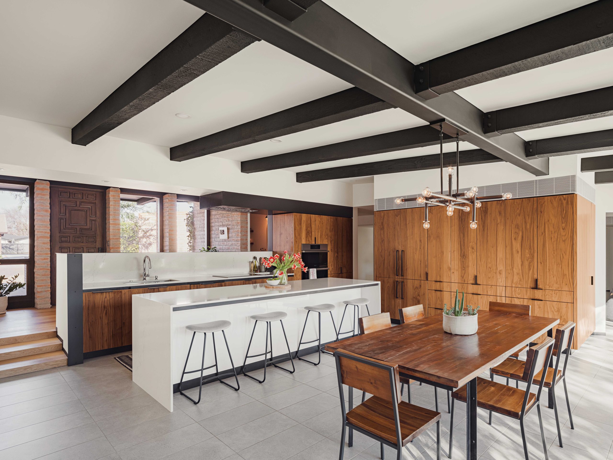 The reimagined kitchen was moved front and center from the original corner space on the right, where new cabinetry fills the void. The kitchen’s placement below the foyer keeps it out of the line of sight from the front door. The subtle black bands beneath the countertops disguise numerous electrical outlets and USB ports. The kitchen hood is part of a black ceiling detail, keeping the view open to the front windows. “When we designed the cabinetry, we thought about adding a walk-in pantry,” says Joanna Noonan. “With a walk-in, you actually lose space because of the floor. Pantry cabinets have more storage.”