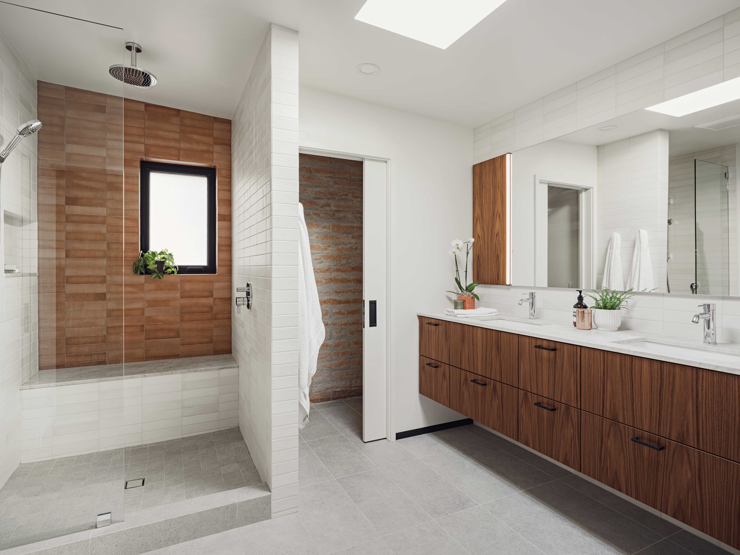 The primary bathroom was reconfigured to include a new shower and bench, with a floating double vanity. The original window was replaced with a black-framed, etched-glass version. “The old layout was choppy,” says Joanna Noonan. “We removed a privacy door that hid the old tub and toilet.”