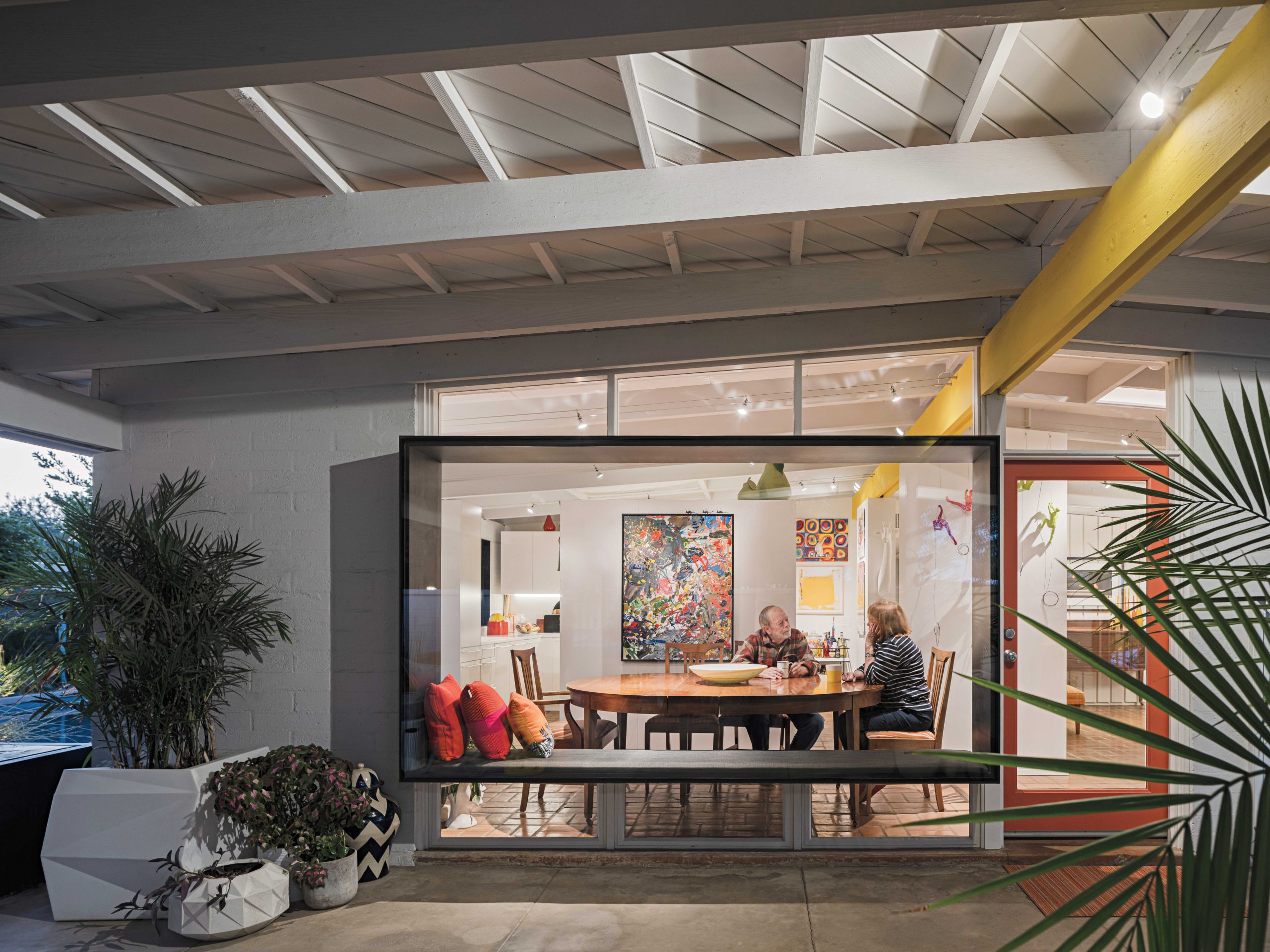 The large bay window adds a dramatic effect to the entryway while honoring Haver’s original design. “One of the big ideas was the insertion of the steel plate frame,” Burnette explains. “The window frames ‘Paintbrush One’ from the entry and incorporates a bench for overflow seating.” The original homeowner had painted the central beam yellow, but the Winkels repainted it a deeper hue to match the yellow kitchen appliances.