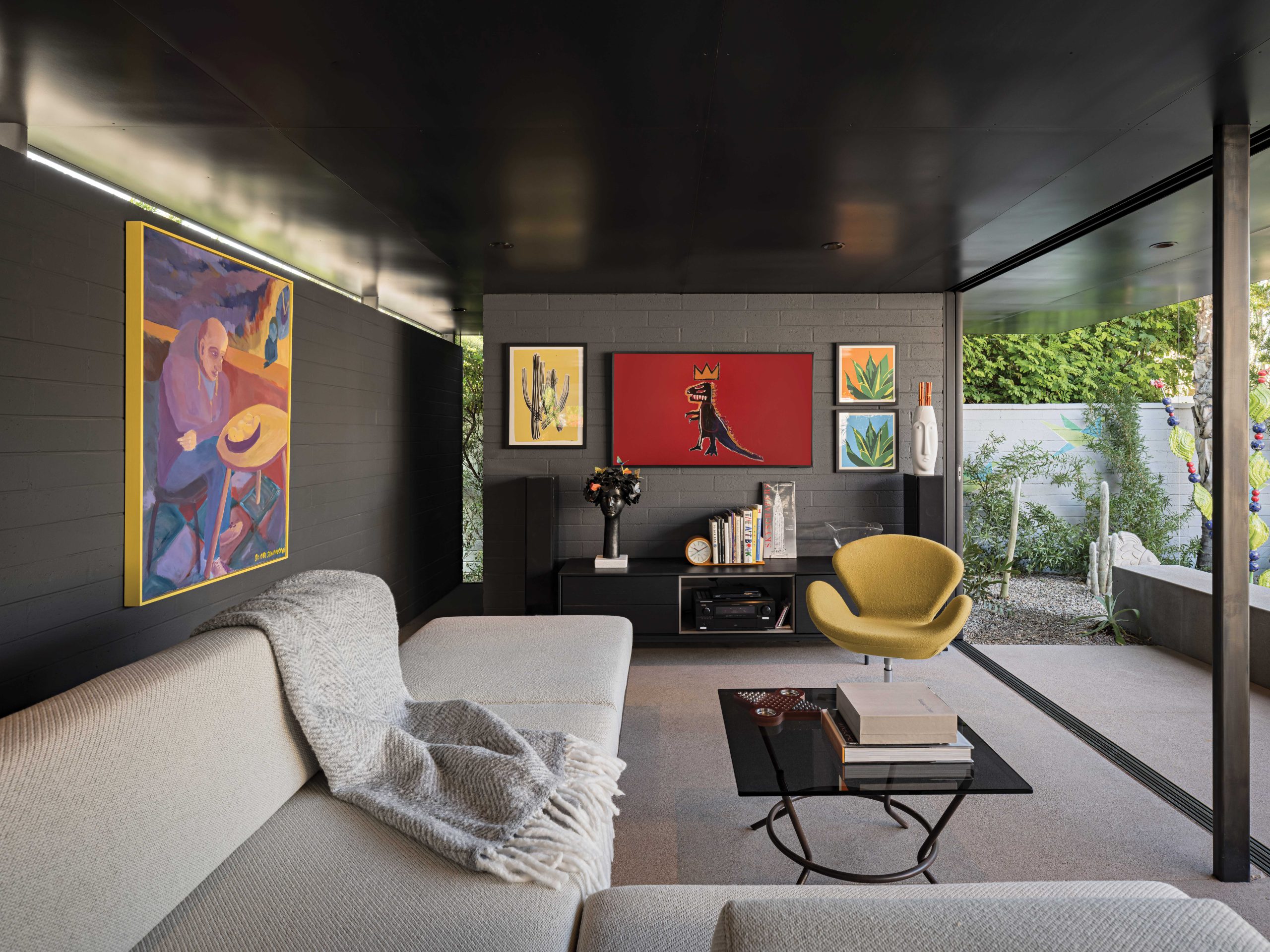 Because the Winkels wanted to remodel their home in a way that would allow for aging in place, Burnette decided to add a casita that can serve not just as a pool house and outdoor entertainment space but also as a guest room for when the grandkids visit and, eventually, a caretaker’s apartment. Narrow clerestory windows separate the steel roof from the dark gray block walls, and a narrow slot window at the end of the hallway lets in additional light. The custom sofa transforms into a queen-size bed, while the TV, when not in use, displays a colorful image by Jean-Michel Basquiat.