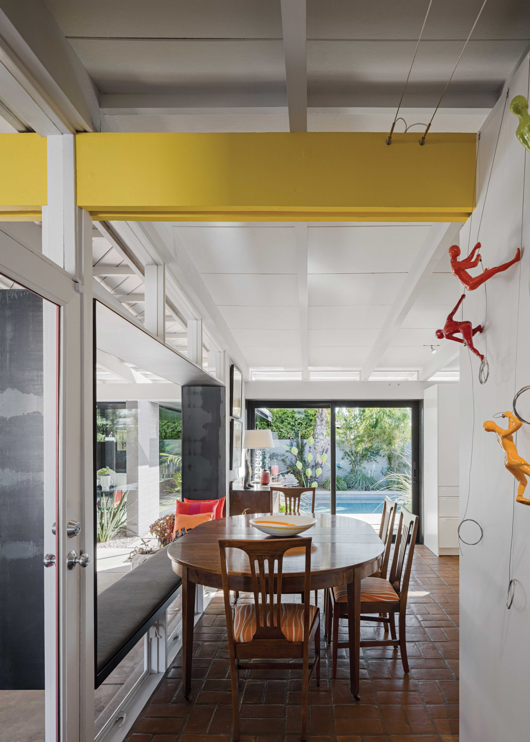 Initially, the Winkels wanted to replace the dining room with a living area so they could look out onto the pool. Instead, Burnette kept the floor plan as is and added a large wall-size sliding glass door that not only physically connects the interior with the pool patio but also opens the line of sight across the main rooms. He framed the doors with contemporary ¼-inch steel plate that pushes outward, making the room feel bigger. He incorporated the same technique on the bay window. The architect replaced the original three-panel center window and wood mullions with a single window, keeping the clerestory windows and lower vent windows. The steel frame serves double duty as bench seating during large parties or when the entire family gathers for meals.