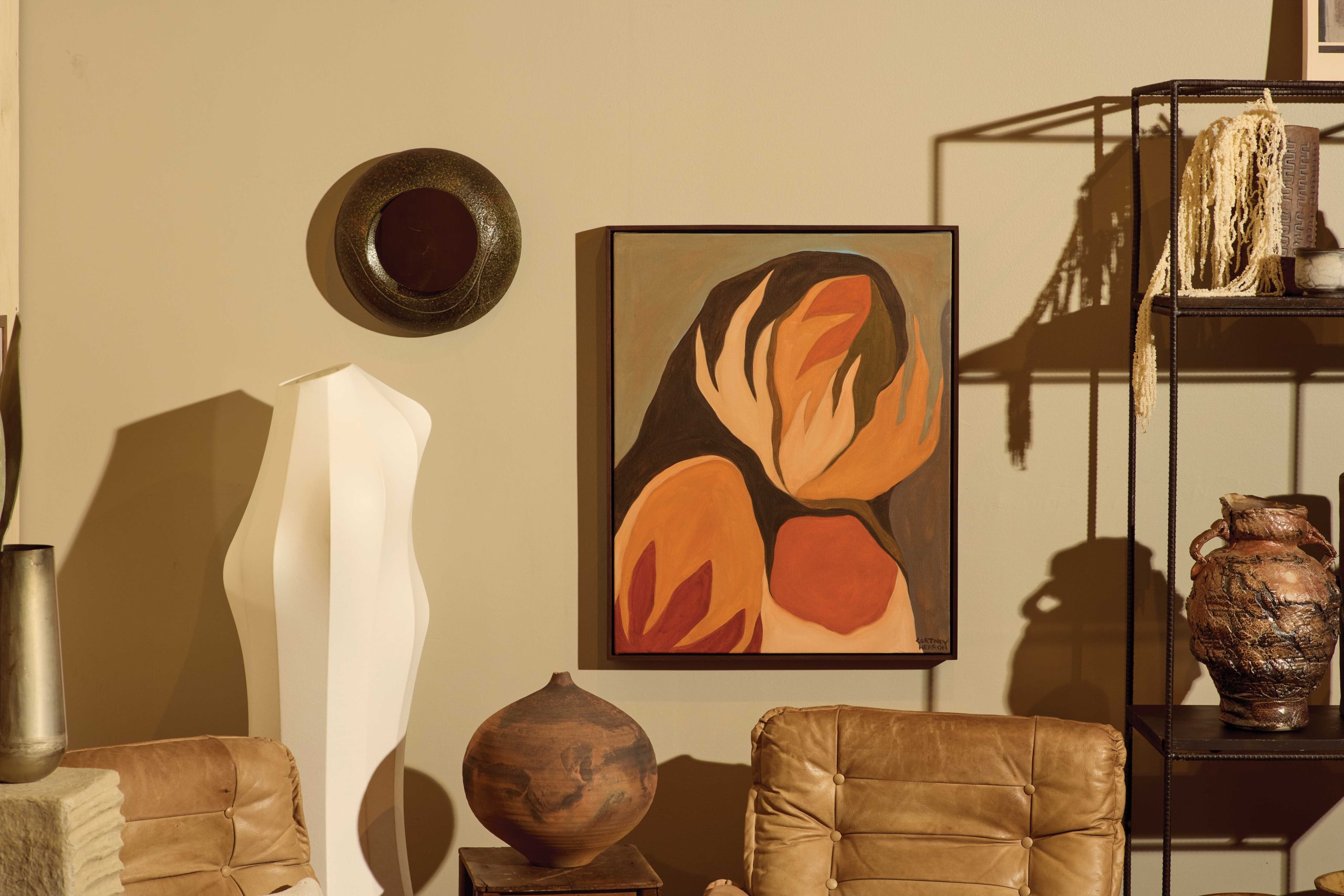 A striking oil painting by Cortney Herron titled “Absorbed Energy” adds a splash of color to the neutral-toned pottery and furniture surrounding it.