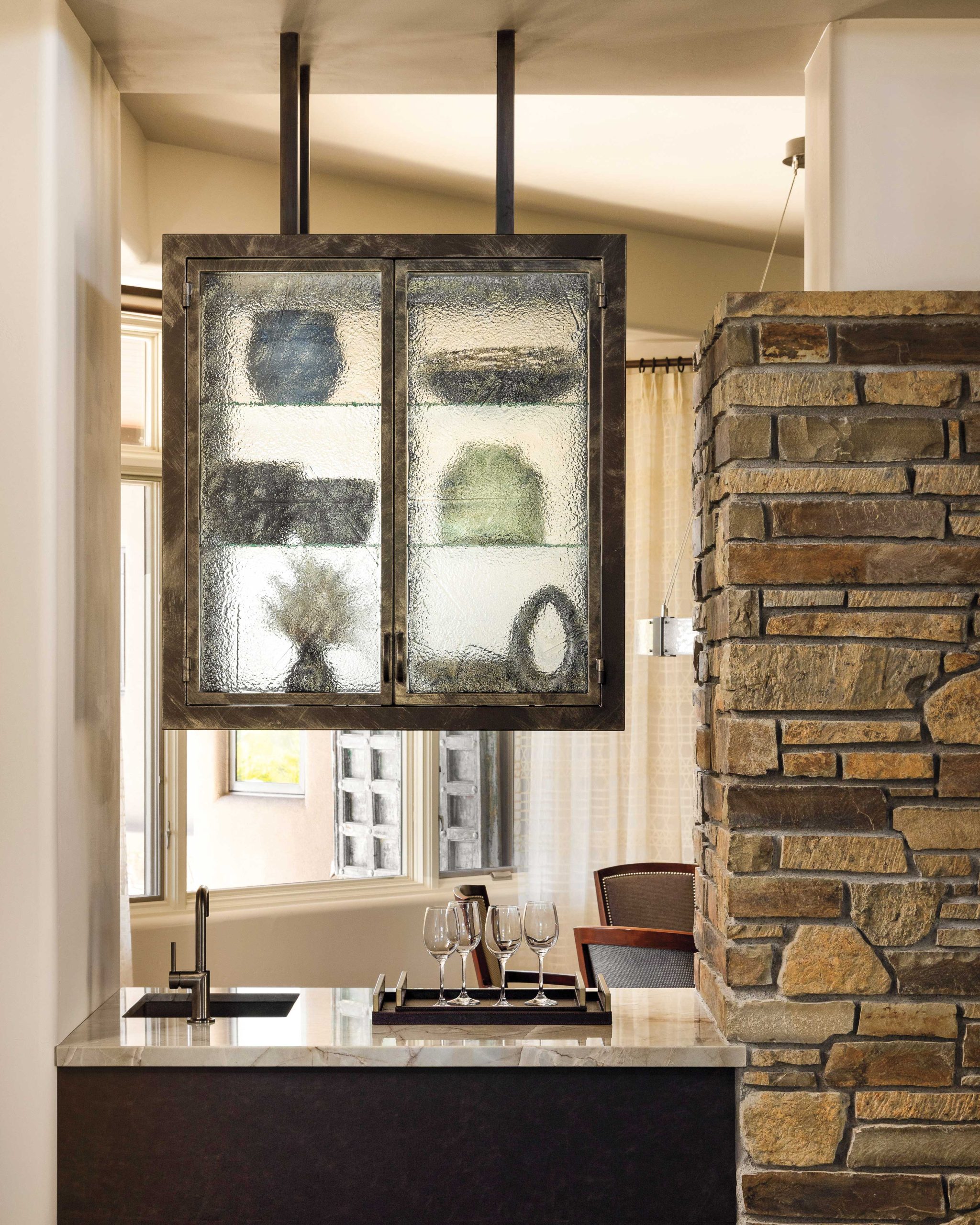 The new hanging steel and glass cabinets between the living area and dining room can be opened from both sides. The interior designer resurfaced the lower cabinetry with a leather veneer for a sophisticated, tactile impact. above A new light fixture and area rug update the dining room, where the original custom cabinet displays tabletop