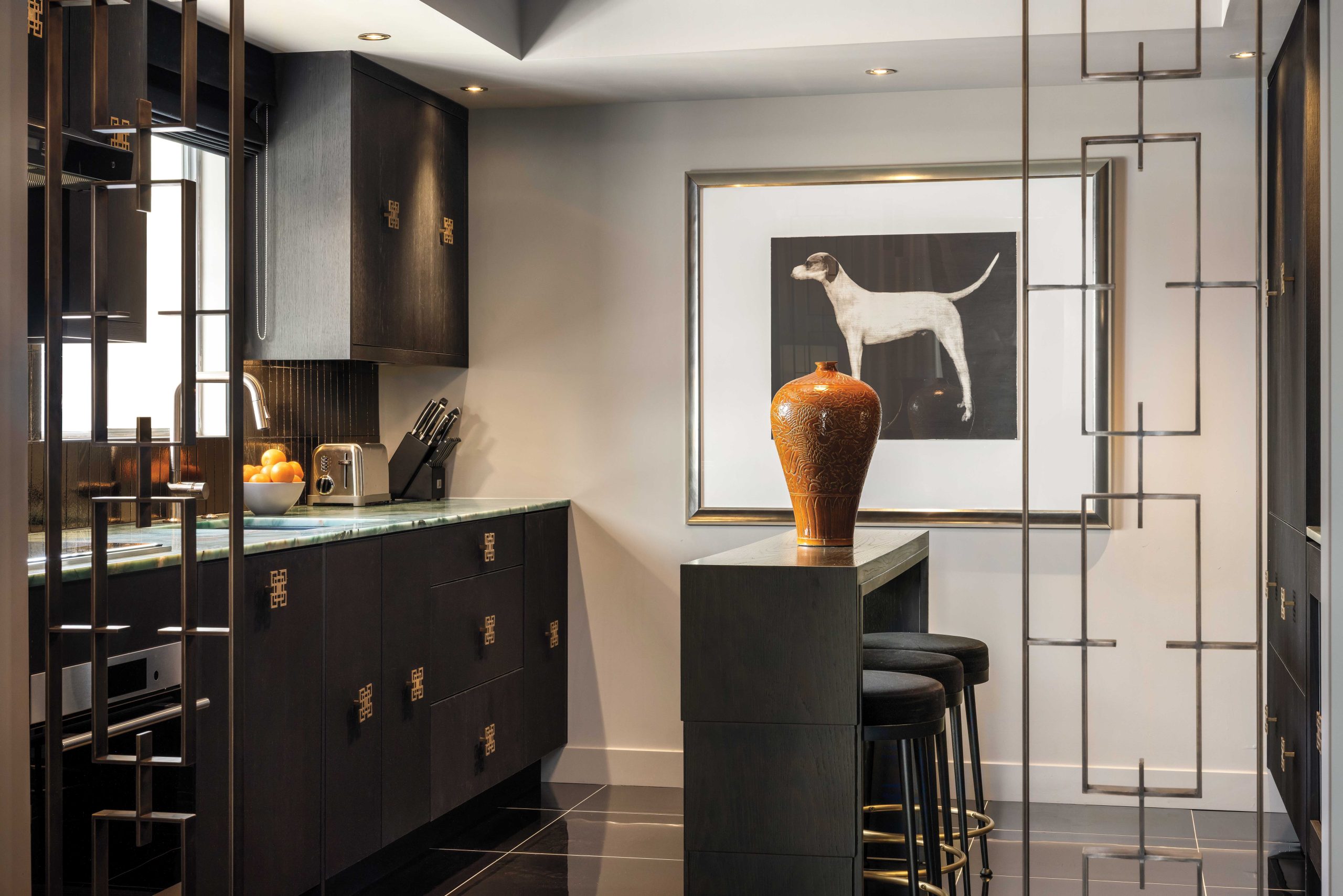 McIntyre commissioned custom brass midcentury-style room dividing screens to provide separation from the dining room and “punctuate the entrance” to the kitchen. Turquoise and green quartzite countertops feel “decidedly 1960s and Asian,” while brass pulls on ebonized oak cabinetry blend Regency and Asian styles. “The kitchen, I hope, feels a bit like a hotel bar,” he says. “I get into the narrative. I get into the fantasy of it.”