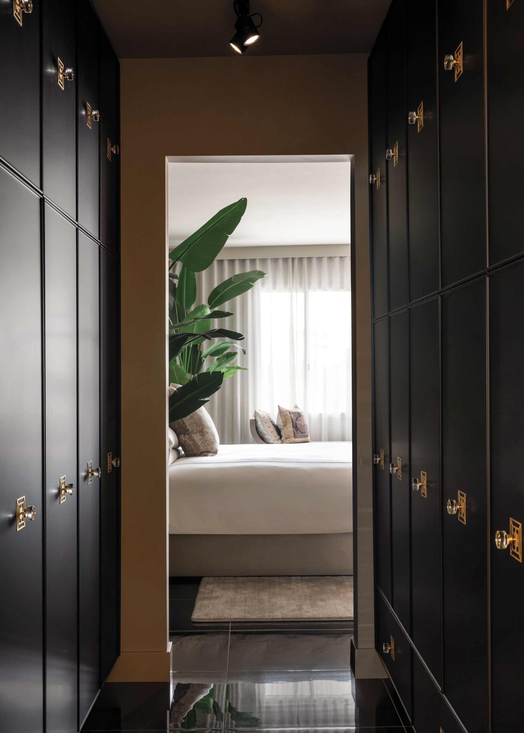 The open walk-through closet from the home’s original 1960s floor plan did not suit McIntyre. “I just couldn’t stand walking past all the clothes and shoes. So, we turned it into a cabinetry-style closet. We decided to do this kind of Asian black art deco paneling with Regency knobs that act like a jewelry detail.” The visual of a long passageway with a curiosity-piquing glimpse into a larger room beyond is reminiscent of the penthouse’s central colonnade.
