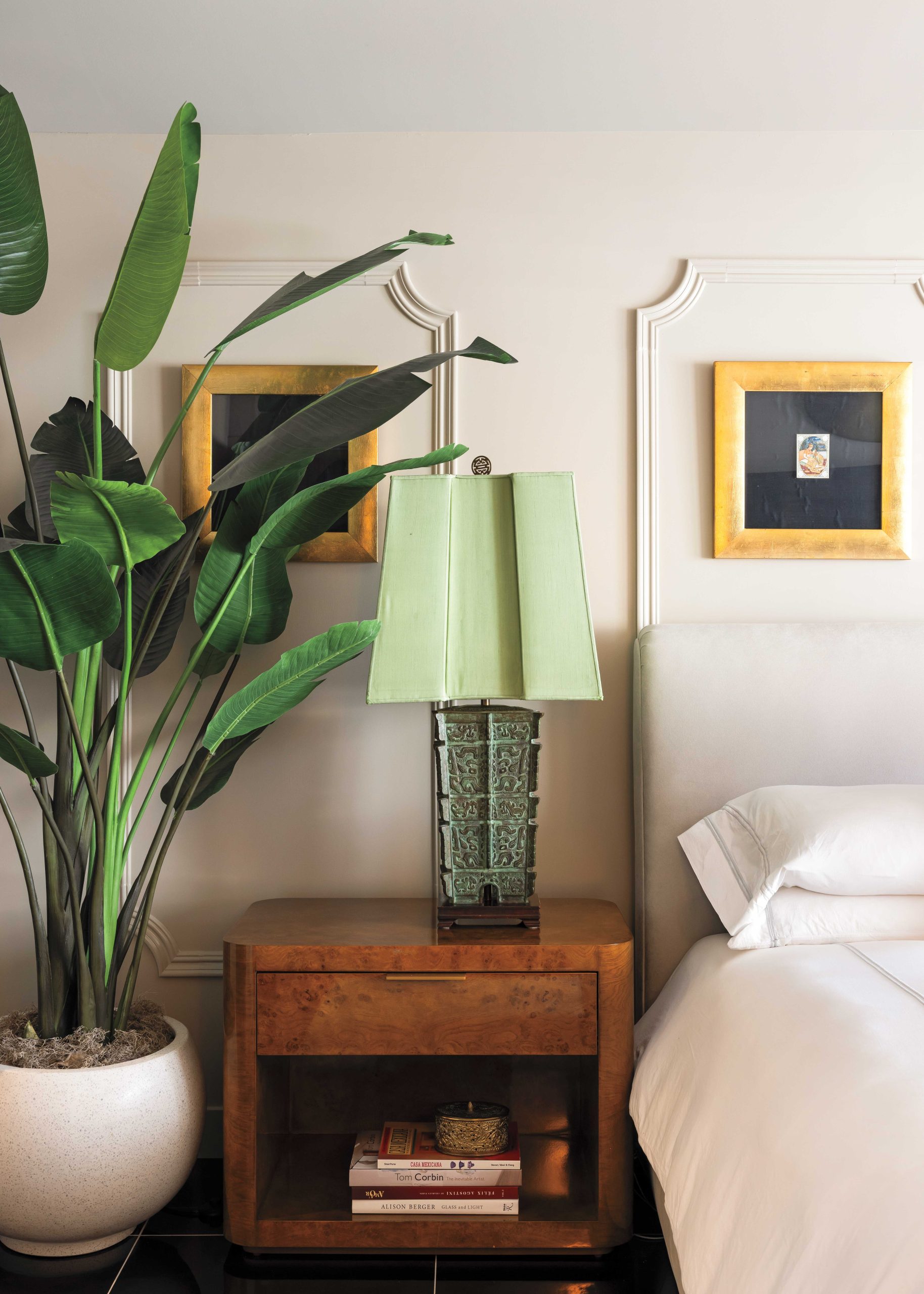 McIntyre always features these antique Indian carvings—framed here in gold—in clusters of four. “We added the paneling on the wall to harken to the 1964 vibe of the place,” he says. “The original homes had moldings going down the hall. It’s a true nod to the original Olympus apartments.” Bronze Hollywood Regency lamps and a tall houseplant pop against the neutral palette with calming green tones.