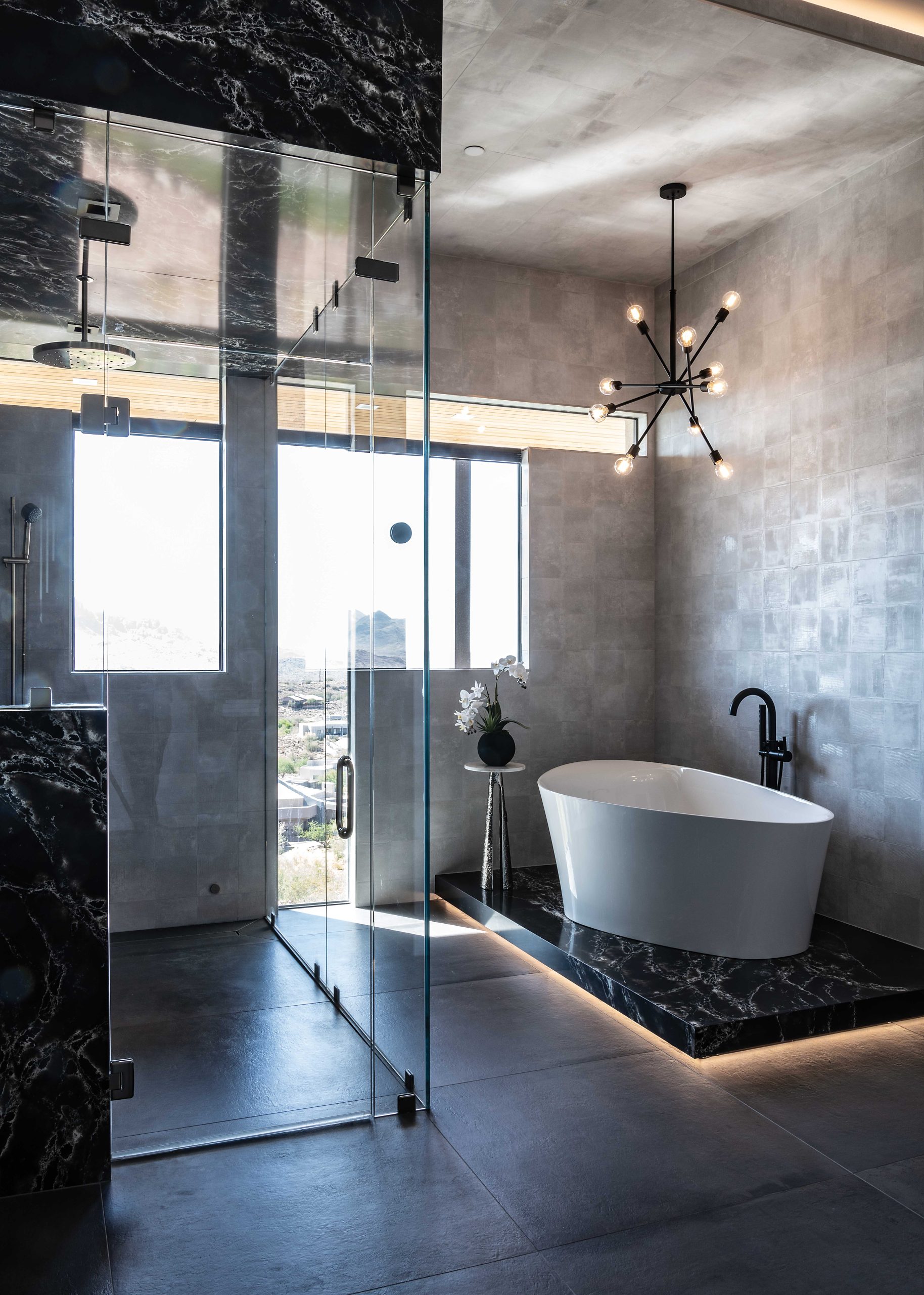 In the primary bath, Marek wrapped the curbless shower in black quartzite slab. The dropped ceiling above the bathtub and adjacent walls are wrapped in cool gray textured tile. “The shape of the tub was important,” the interior designer recalls. “We didn’t want a standard oval tub, we needed something a little more edgy in that area. It gives it another architectural pop.”