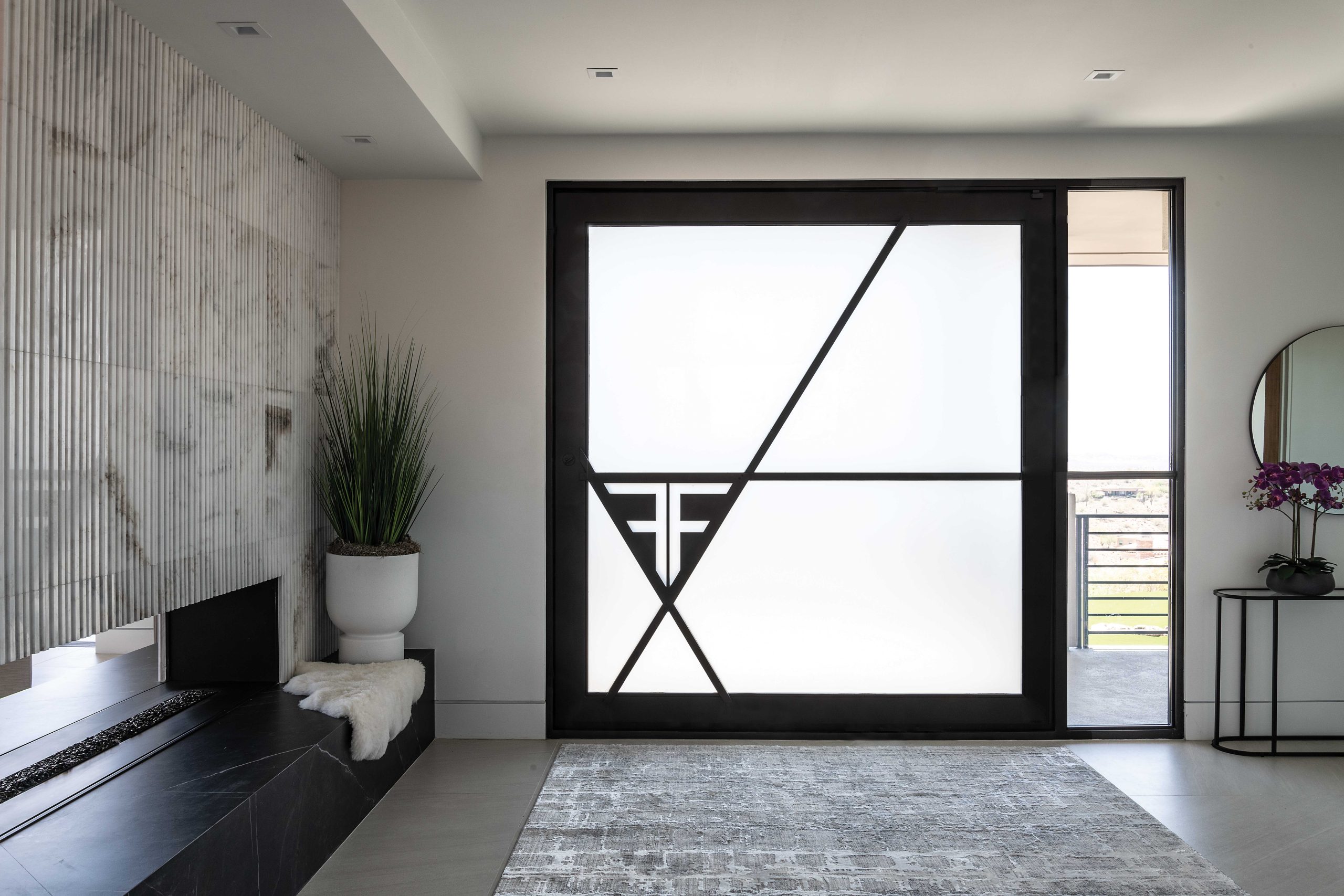 The custom 8-foot-square front door incorporates the homeowner’s initials. Frosted glass provides privacy and reduces glare. The three-sided fireplace creates a statement at the entry and provides separation from the adjacent great room to the left.