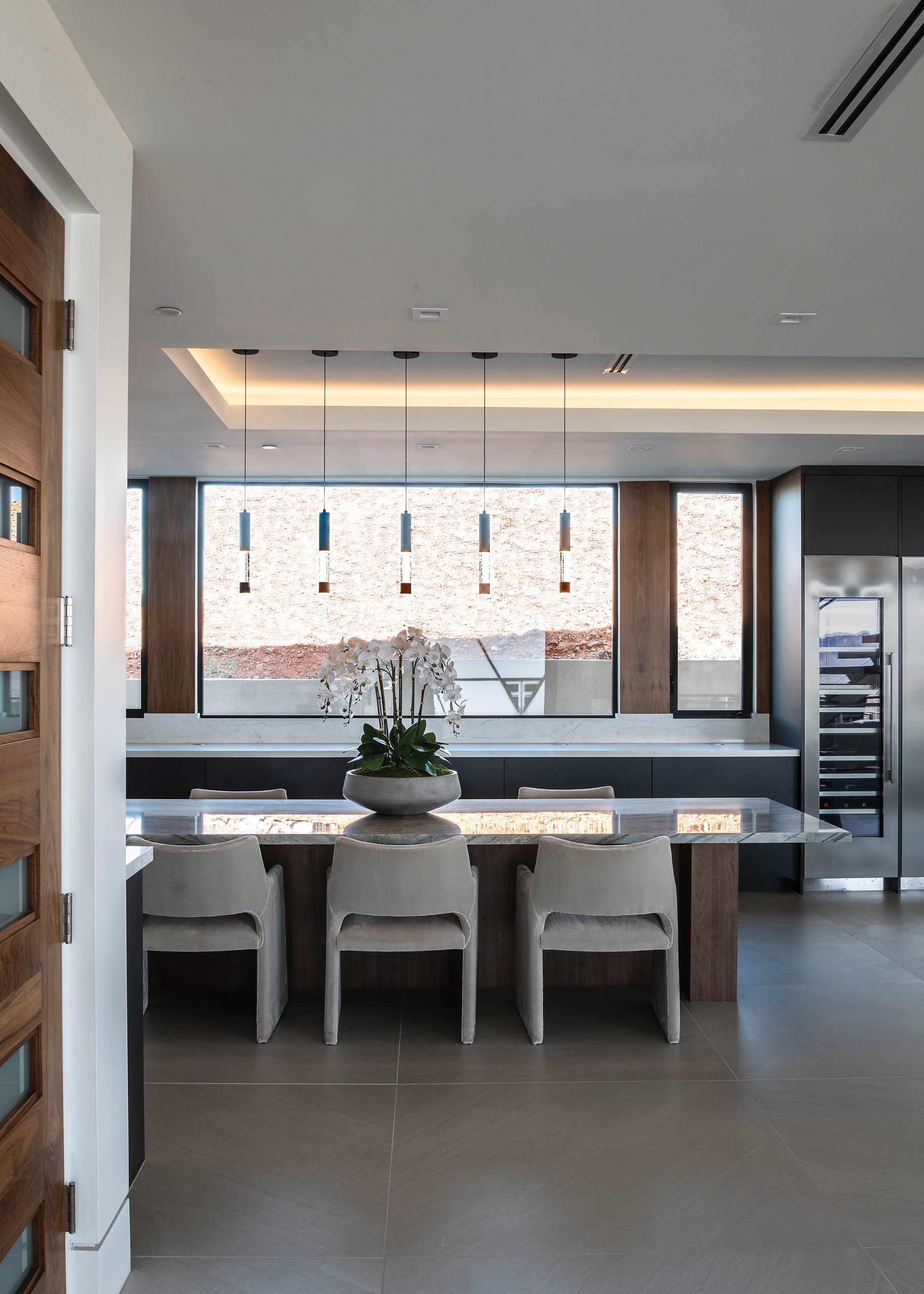 A built-in dining table topped with the same slab as the island is part of the kitchen experience. Through the window, the rocky peak of the mountain on which the home sits is visible.