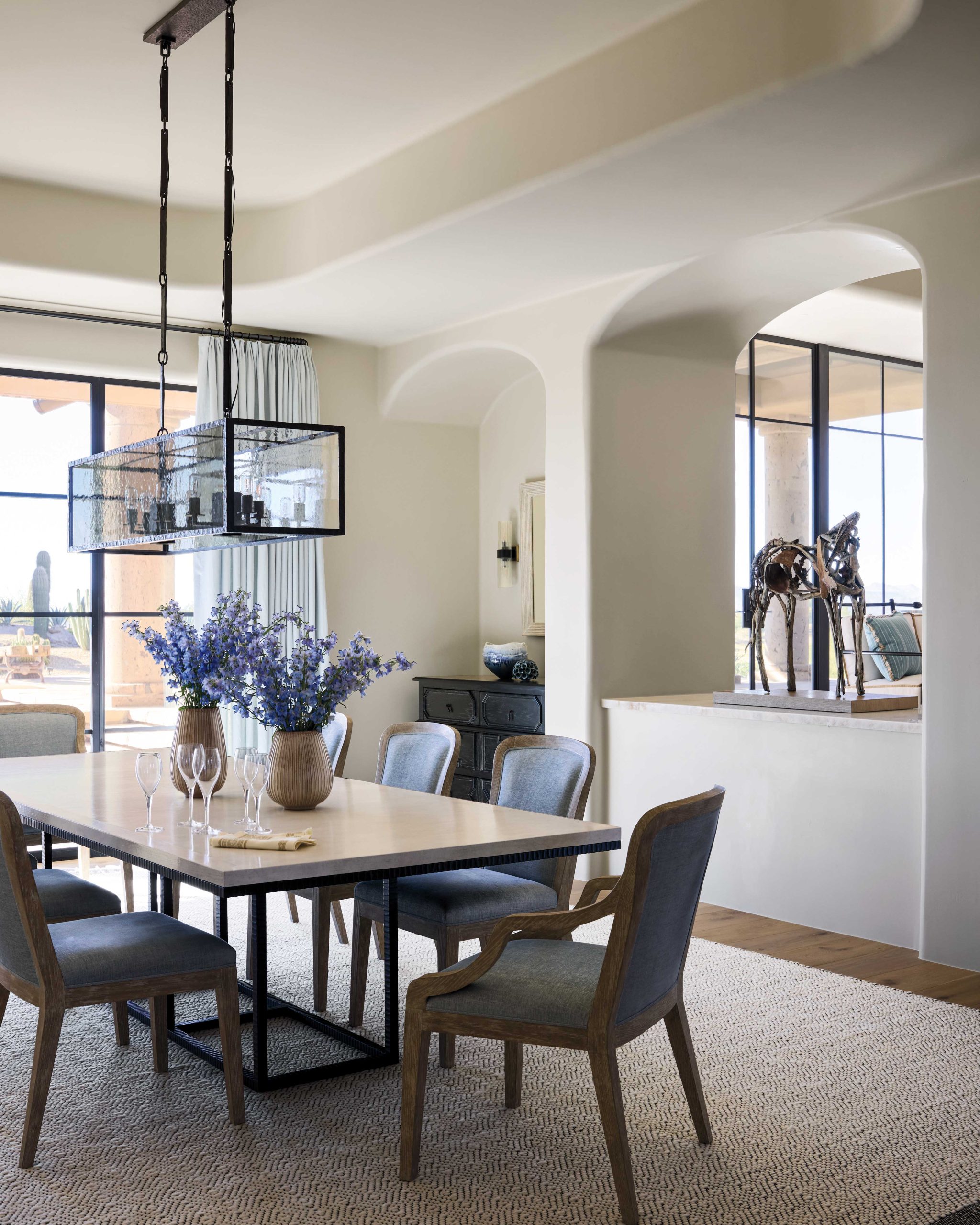 New arched openings connect the dining area to the living room. Sharpe paired an edgy table with chairs that bear a Spanish Colonial silhouette as a nod to the home’s transition. Pale draperies soften the look.